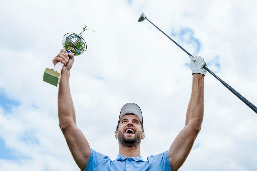 Happy golf tournament winner with trophy in the air