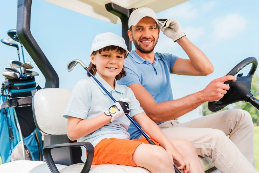 Happy young boy in golf cart with dad