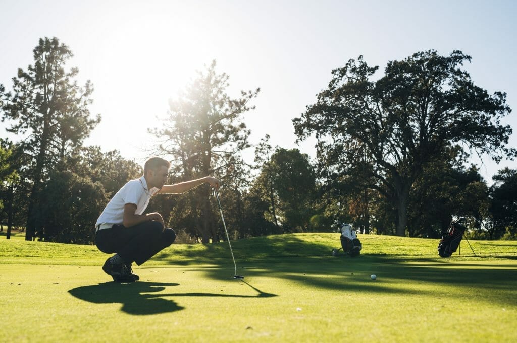 Man reading putt with sunset in background