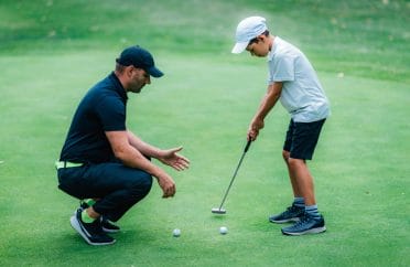 Golf instructor teaching young boy putting