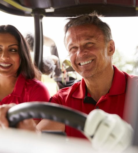 Happy couple playing golf while driving cart